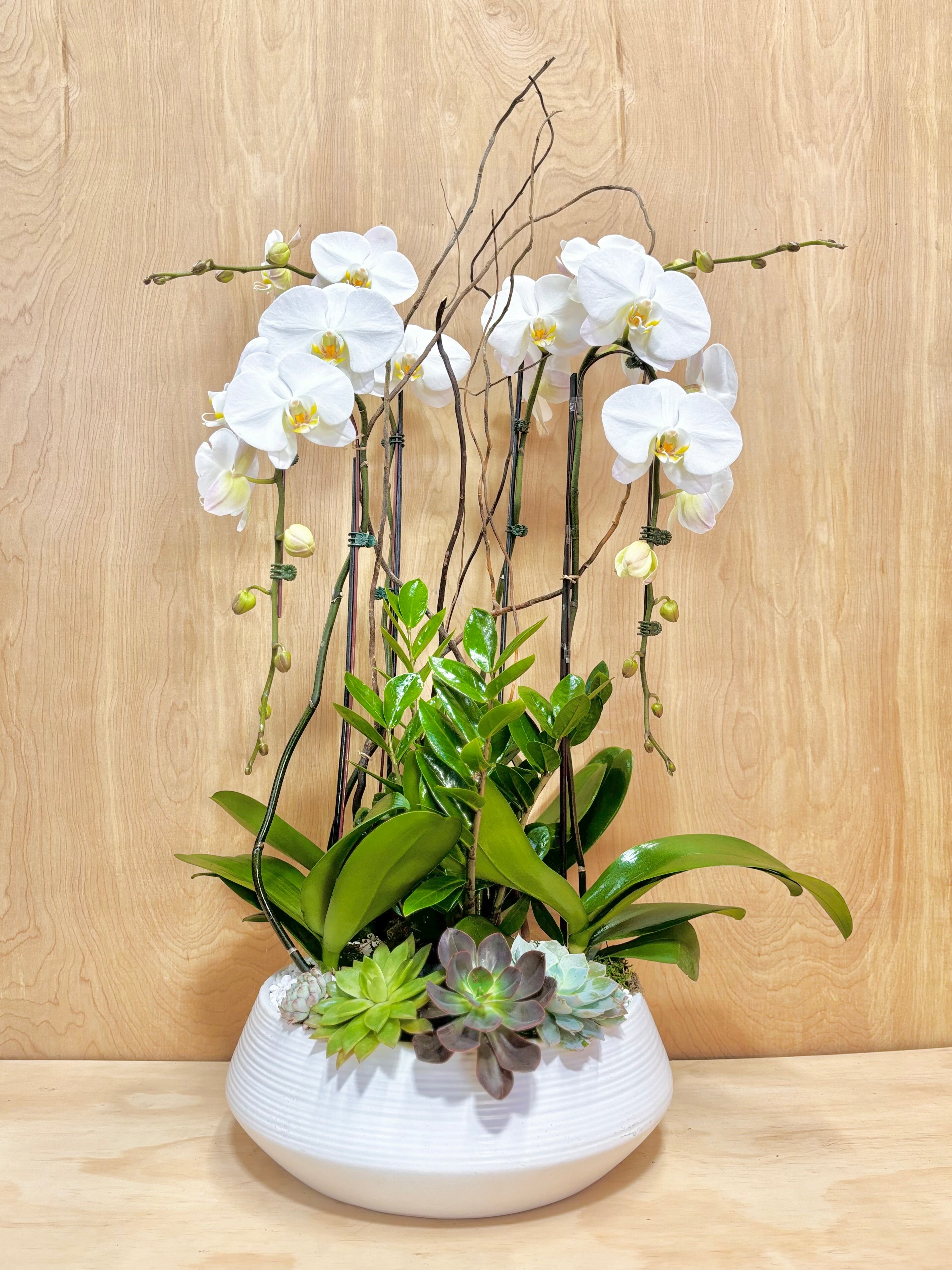 Floral arrangement with white flowers and greenery in a white vase on a wooden surface.