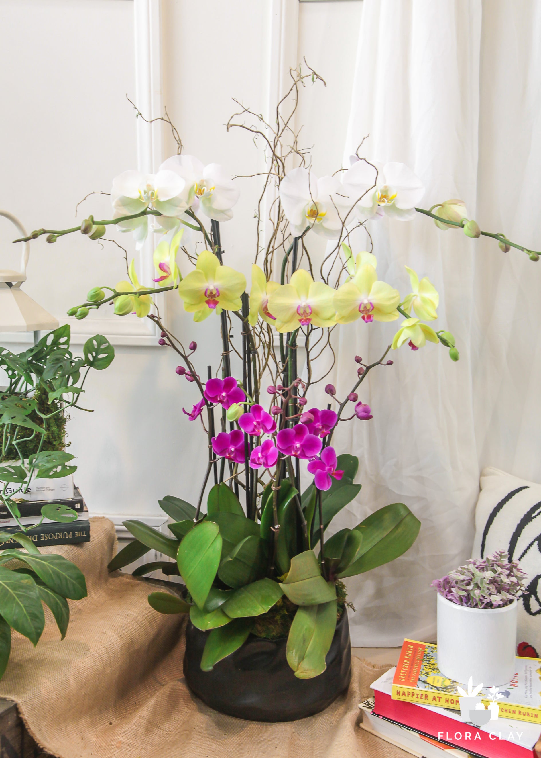 A colorful floral arrangement featuring white, orange, and pink orchids in a wooden vase, placed on a table with a blurred background.